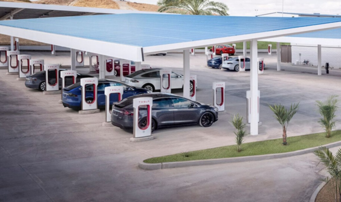 En modern Tesla Supercharger station med ett blått solpanelstak och flera Teslor som laddar.